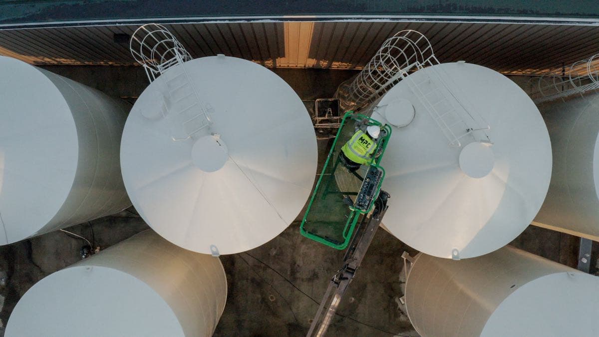 Overhead view of MPC worker between massive industrial storage tanks